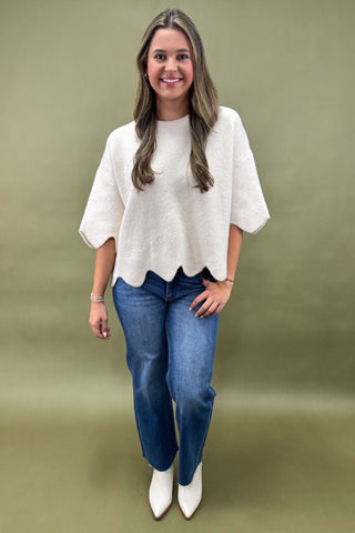 Woman wearing a white blouse, blue jeans, and white shoes on a green background