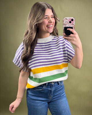 Woman taking a selfie wearing a colorful striped sweater against a green background
