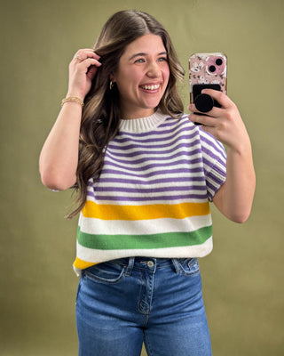 Woman taking a selfie wearing a colorful striped sweater and blue jeans on a green background