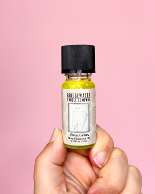 Bottle of Bridgewater Candle Company Sweet Grass perfume oil held against a pink background