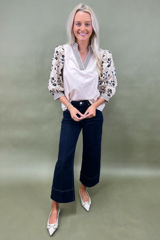 Woman wearing a patterned blouse and dark jeans on a green background