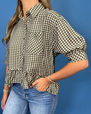A woman wearing a brown and white gingham check short-sleeve blouse with puff sleeves and a ruffled hem, paired with blue jeans