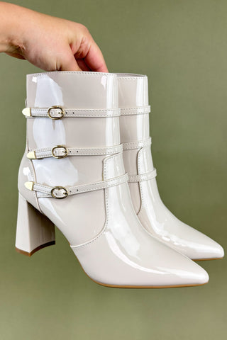White patent leather boots with gold buckles held against a green background