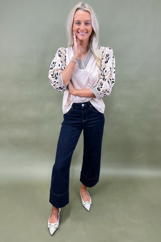 Woman wearing a patterned blouse and dark jeans on a green background