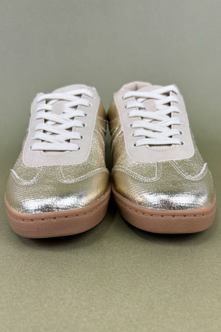 Pair of metallic gold sneakers with white laces on a neutral background