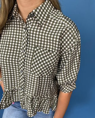 A woman wearing a short-sleeve button-up shirt with a brown and white gingham check pattern and a ruffled hem