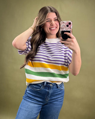 Woman taking a selfie wearing a colorful striped sweater and blue jeans on a green background