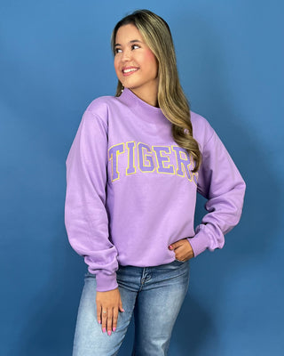 A woman wearing a lavender purple sweatshirt with 'TIGER' printed in yellow and blue varsity lettering