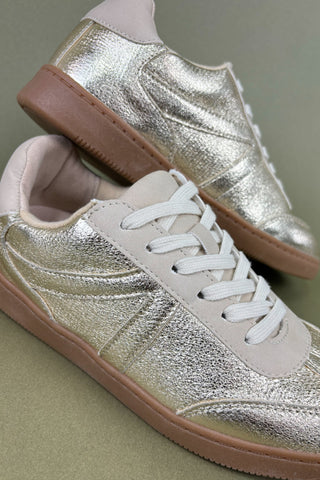 Pair of silver glittery sneakers with brown soles on a neutral background
