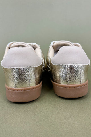 Pair of metallic gold sneakers with beige soles on a green background