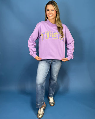 A woman modeling a lavender purple sweatshirt with 'TIGERS' printed across the chest in yellow and white