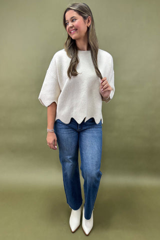 Woman wearing a white scalloped hem top and blue jeans on a green background