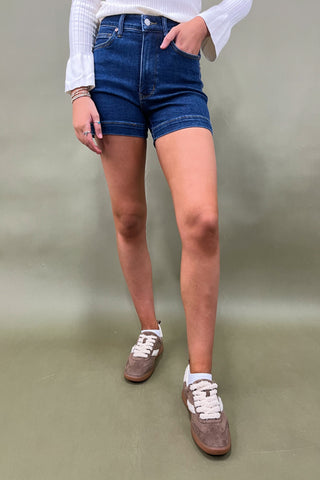 Person wearing blue denim shorts and brown shoes on a plain background