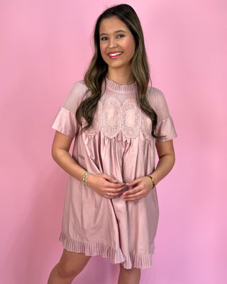 Woman wearing a pink dress with lace details against a pink background