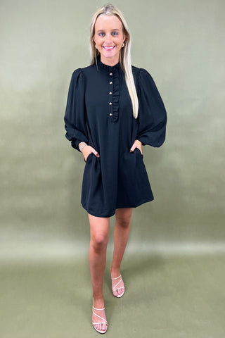 Woman wearing a black dress with long sleeves against a green background