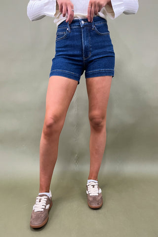 Person wearing blue denim shorts and white sneakers on a plain background