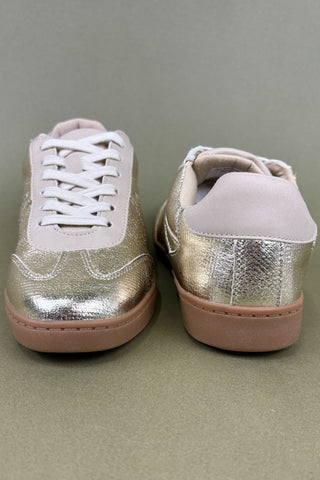 Pair of metallic gold sneakers with white laces on a gray background
