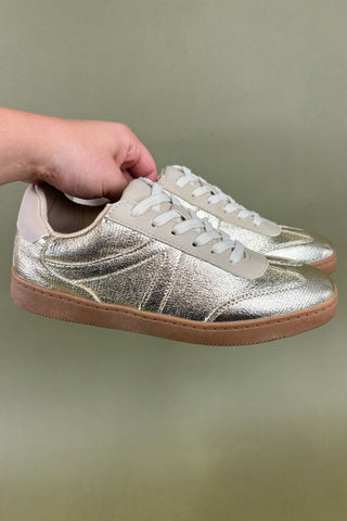 Silver glitter sneakers with brown soles held by a hand against a plain background