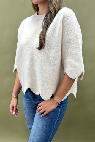 Person wearing a white poncho and blue jeans against a green background