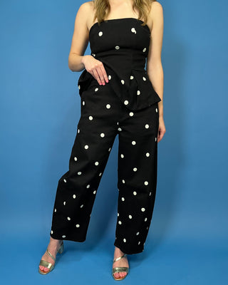 Black strapless polka dot peplum jumpsuit with a fitted bodice and flowy wide-leg pants.
