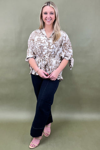 Woman wearing a patterned blouse and dark pants against a green background