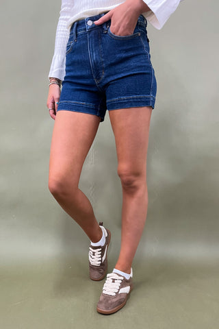 Person wearing blue denim shorts and brown sneakers on a plain background
