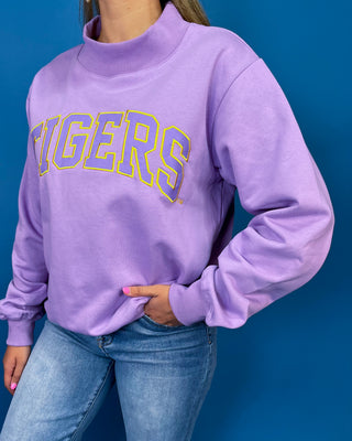 A person wearing a lavender purple sweatshirt with 'TIGERS' printed across the chest in purple and yellow