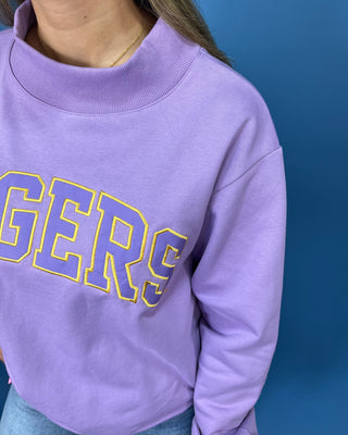 A close-up of a person wearing a lavender purple crewneck sweatshirt with 'GERS' printed across the chest in yellow varsity block letters