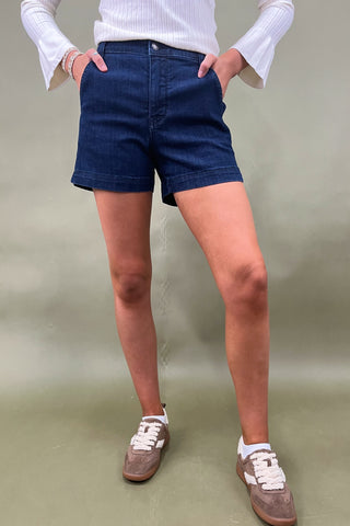 Person wearing blue shorts and white sneakers on a plain background