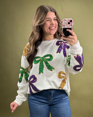 Woman wearing a festive sweater with colorful bows, taking a selfie against a green background.