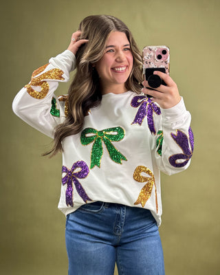Person wearing a white sweater with colorful sequin designs on a gold background