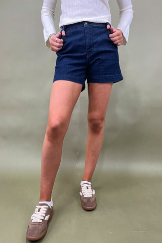 Person wearing blue shorts and white sneakers on a plain background