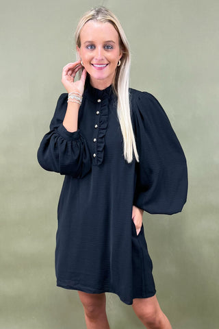Woman wearing a black dress with long sleeves against a green background