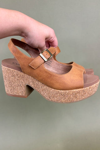 Brown cork sandal with a buckle held by a hand on a plain background