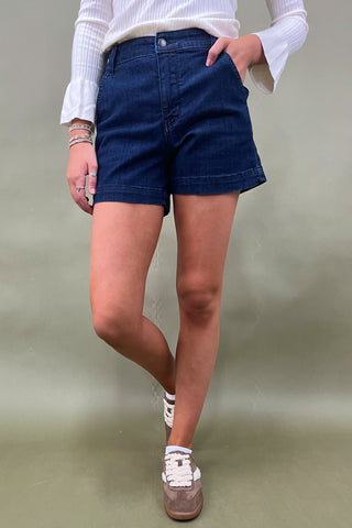 Person wearing blue shorts and a white top against a plain background