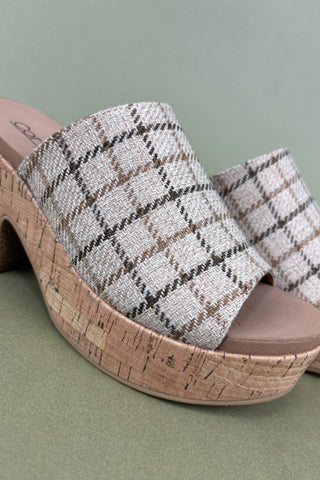 Plaid patterned slide sandal with cork wedge sole on a green background