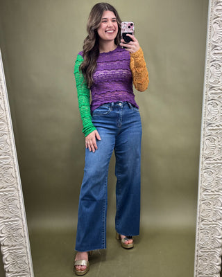 Woman taking a mirror selfie wearing a colorful sweater and blue jeans on a green background