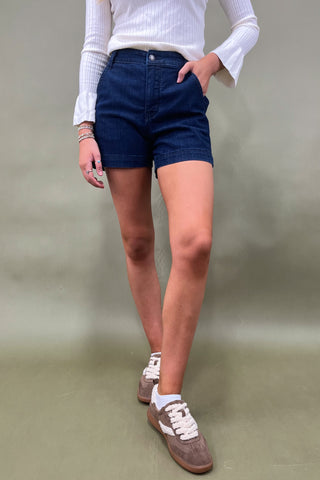 Person wearing blue shorts and white sneakers on a plain background