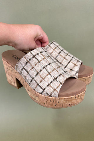 Woven slide sandal with cork sole held by a hand against a green background
