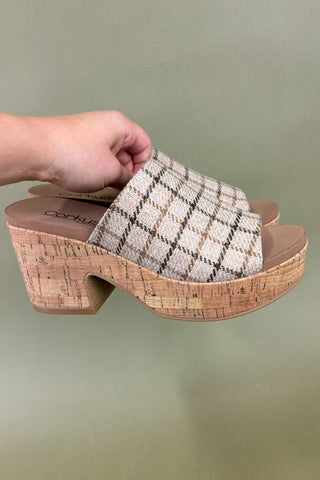 Plaid sandal with cork platform held by a hand against a green background