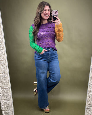 Woman taking a mirror selfie wearing a colorful sweater and blue jeans on a green background