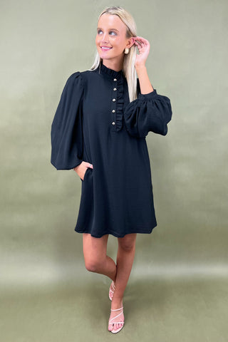 Woman wearing a black dress with long sleeves against a green background
