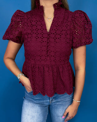 A woman wearing a burgundy eyelet lace blouse with puff sleeves and a scalloped hem