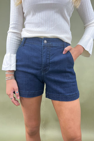 Person wearing blue denim shorts and a white ribbed top against a neutral background