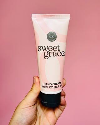 Hand holding a tube of sweet grace hand cream against a pink background