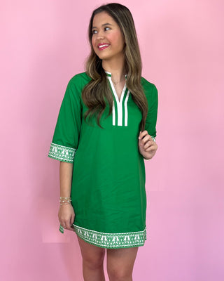 Woman wearing a green dress with white trim against a pink background
