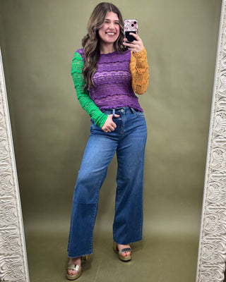 Woman taking a mirror selfie wearing a colorful sweater and blue jeans on a green background