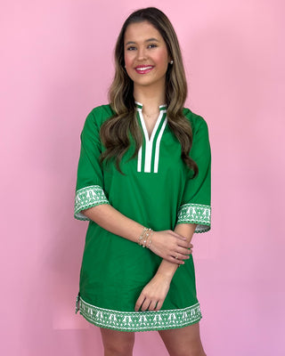 Woman wearing a green dress with white trim against a pink background