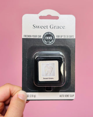 Sweet Grace car air freshener clip in packaging held by a hand against a pink background