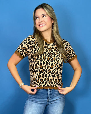 A woman modeling a short-sleeve leopard print top with brown trim, paired with blue jeans